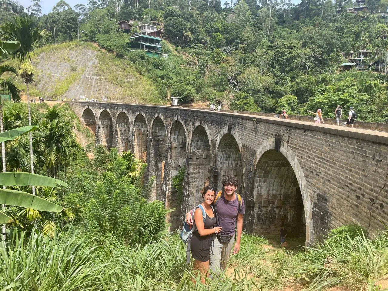Two guests standing on the grassy slope in front of Nine Arch Bridge in Ella