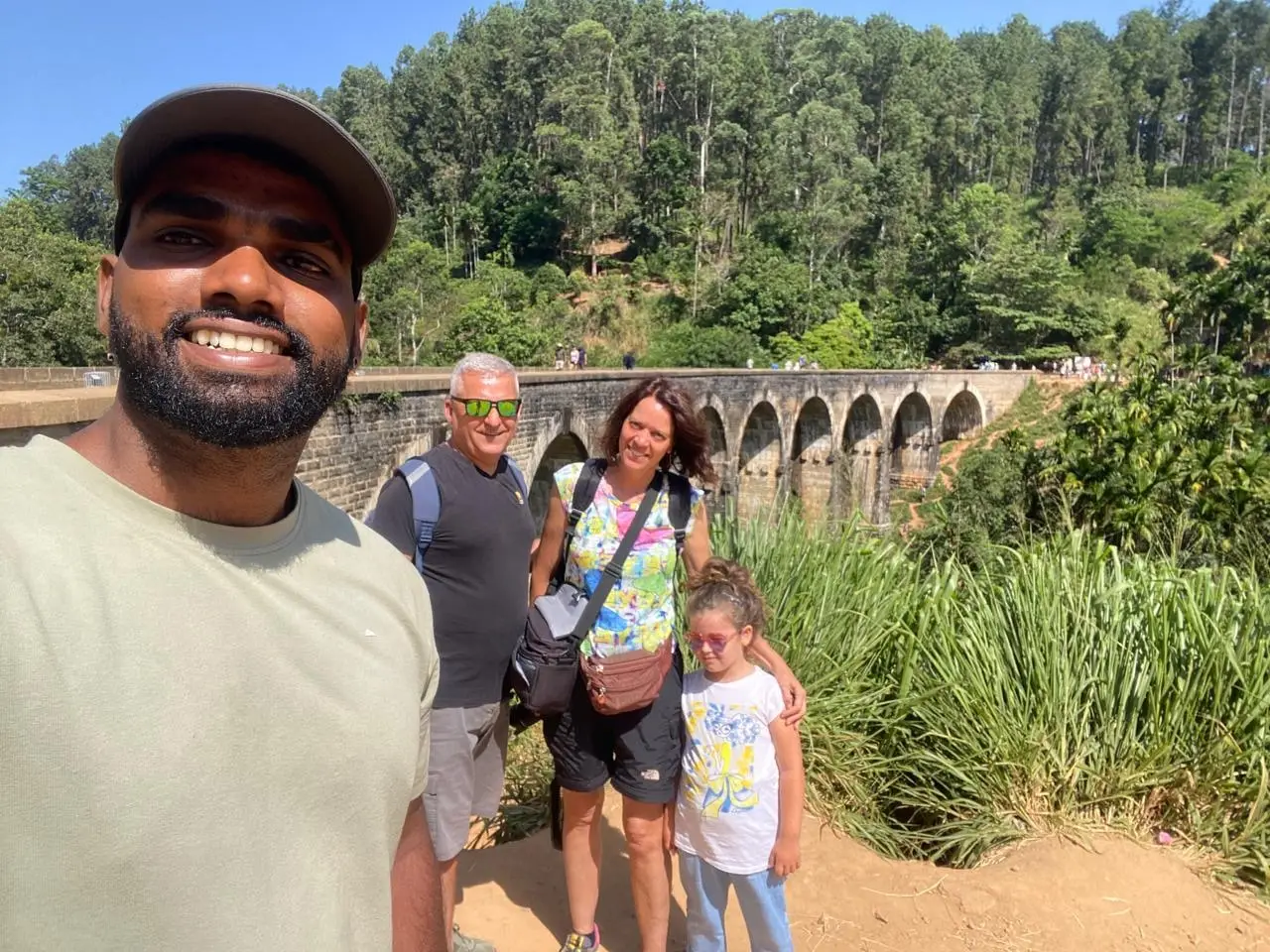 Naveen and three guests on the path below Nine Arch Bridge, the stone arches and jungle behind them