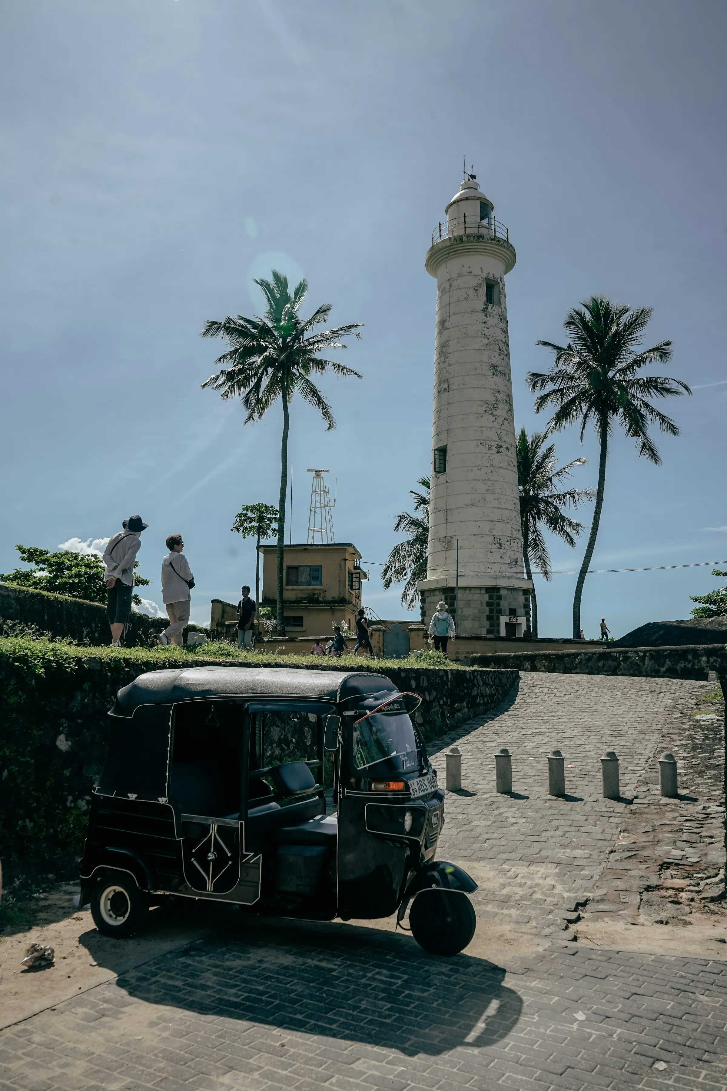 A tuk-tuk parked on a quiet street in front of the white Galle Fort lighthouse