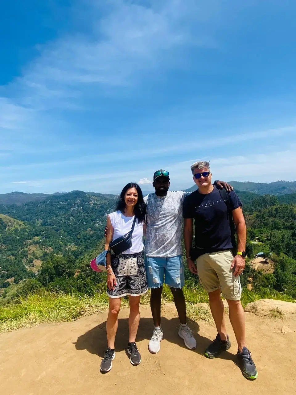 Three guests at a hill-country viewpoint with a wooded valley falling away behind them