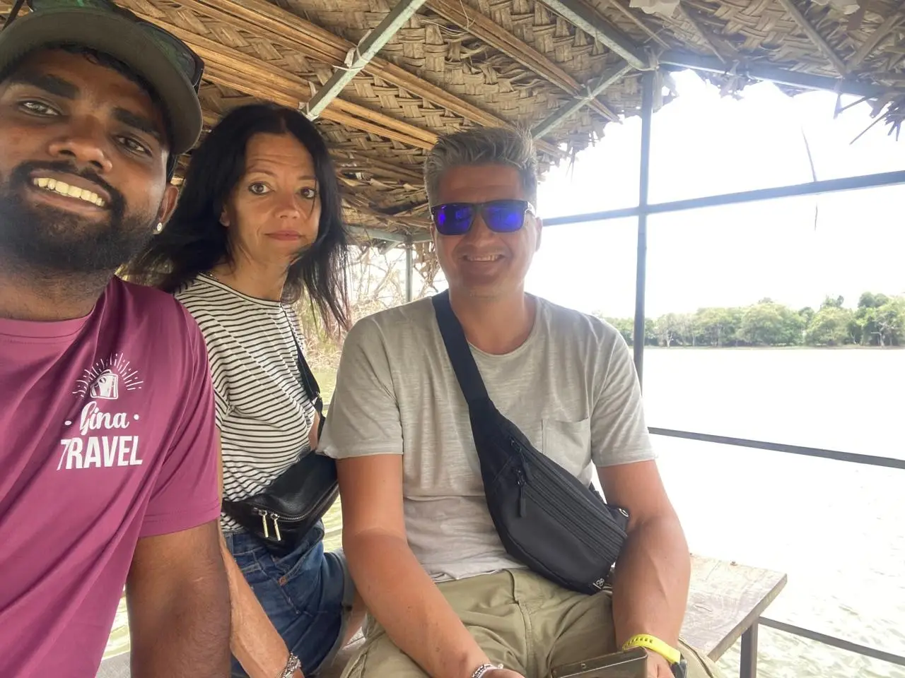 Naveen with two guests under a thatched shelter looking out over a lake