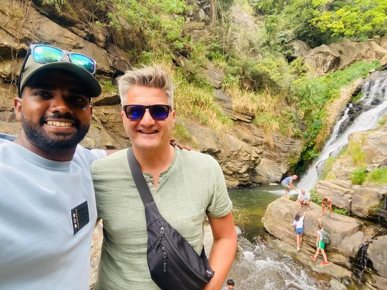 Naveen and a guest in front of a waterfall running down dark rock
